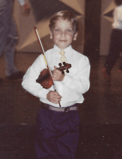 A young boy holding a violin in front of other people.