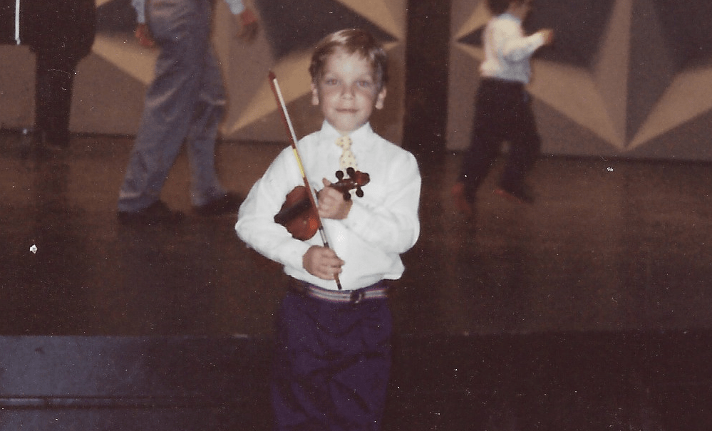 A young boy holding a violin in front of other people.