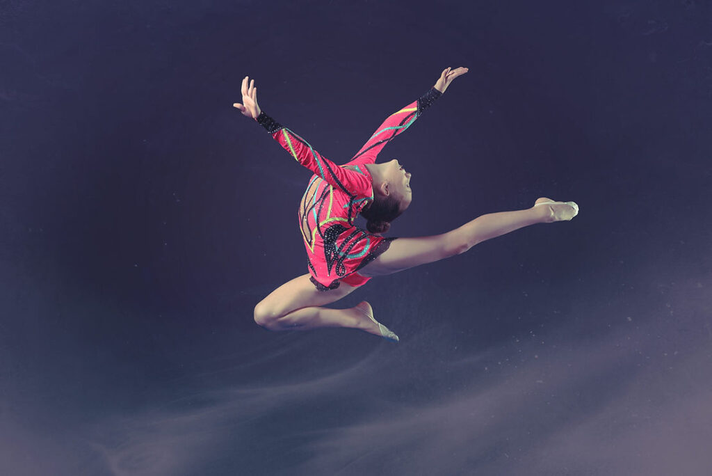 A woman in pink leotard jumping high into the air.