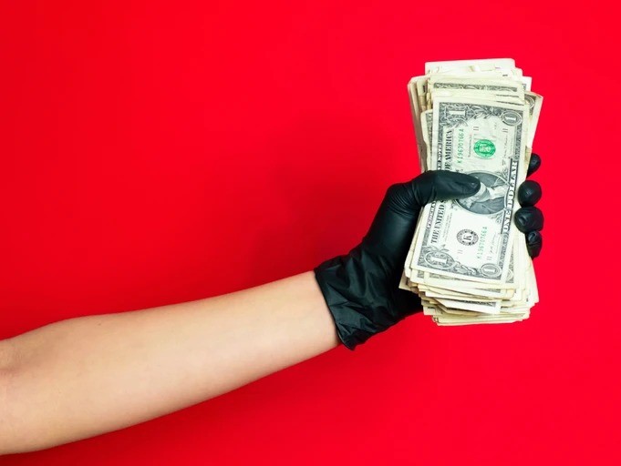 A person holding money in their hand wearing black gloves.