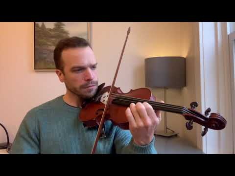 A man playing the violin in front of a lamp.