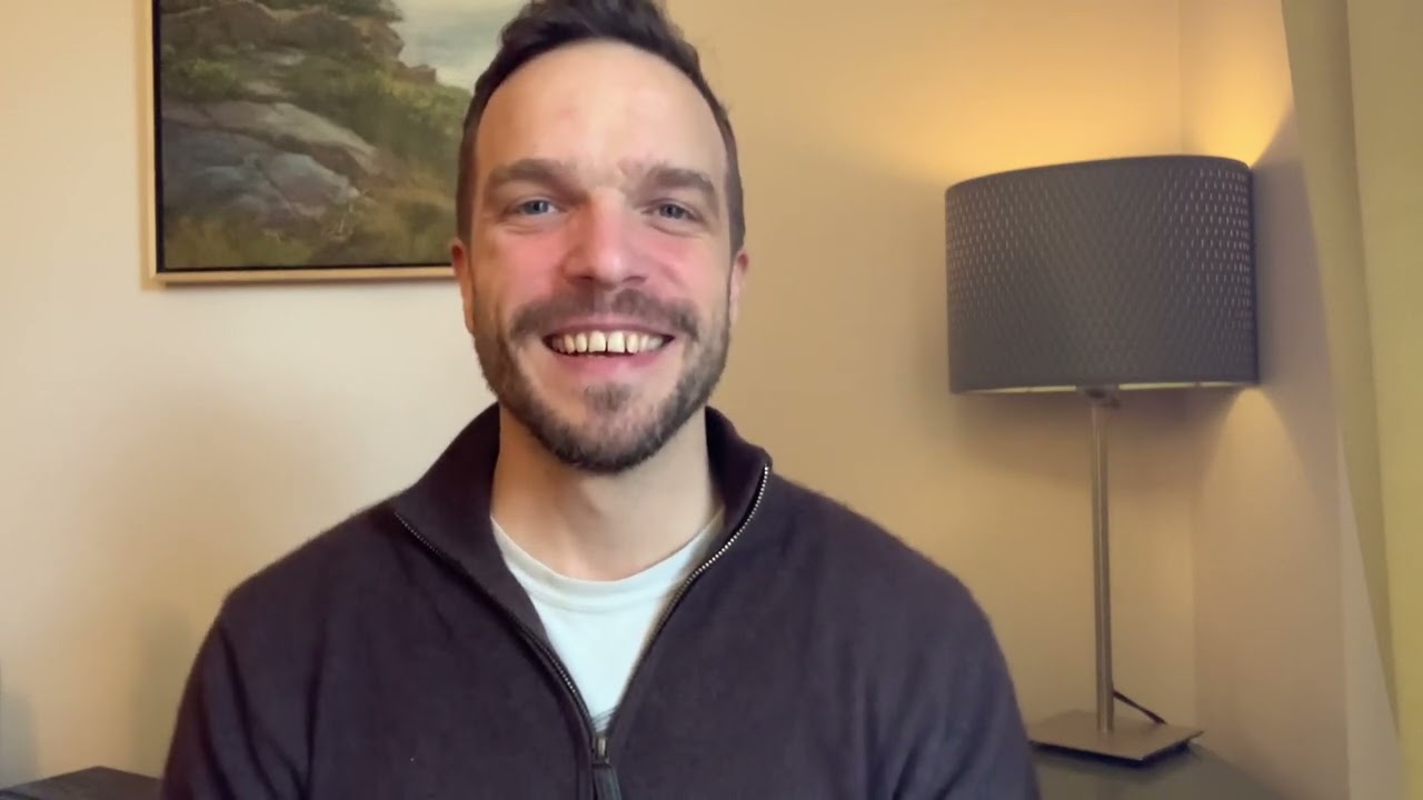 A man smiling for the camera in front of a painting.