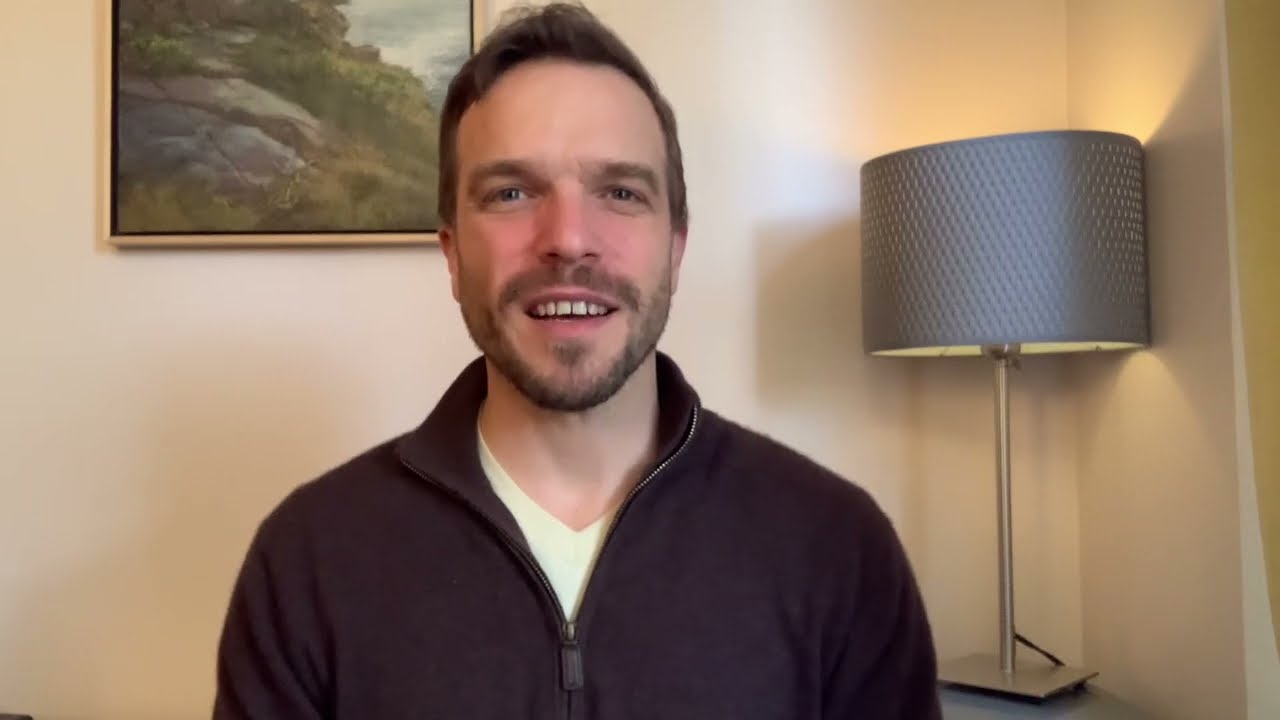 A man in a brown jacket smiling for the camera.