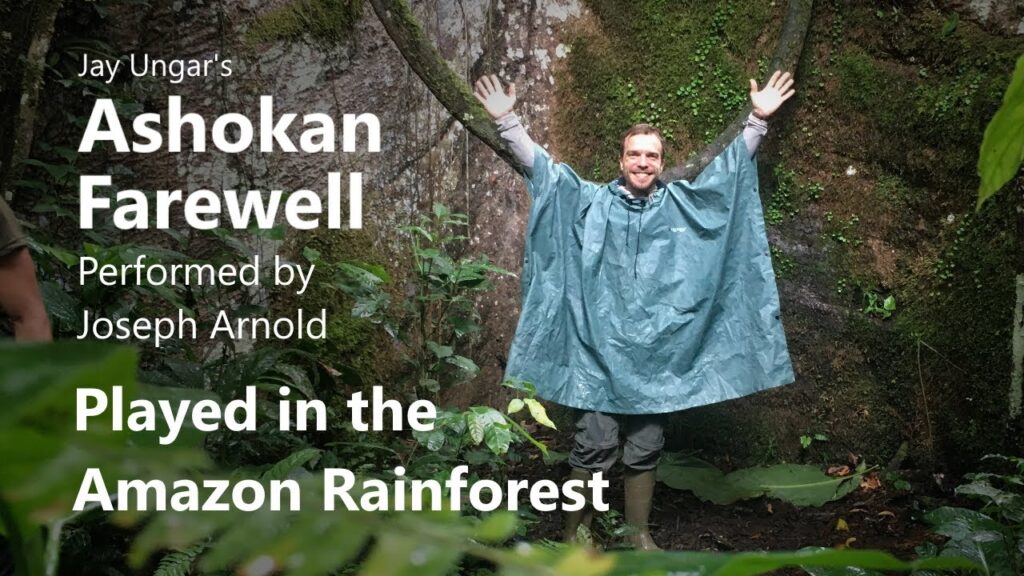 A man in a rain coat standing next to a tree.