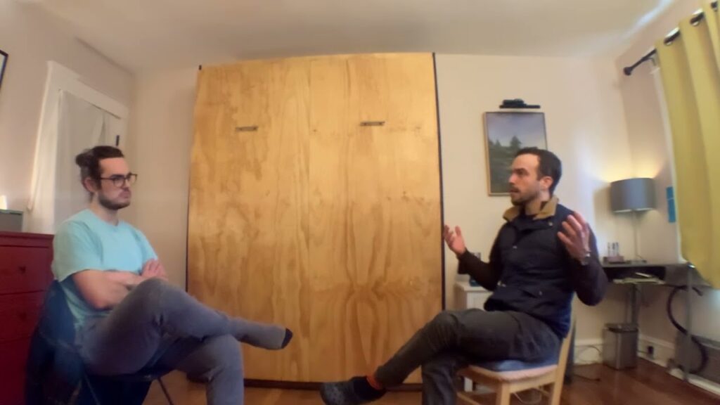 Two men sitting in a room talking to each other.