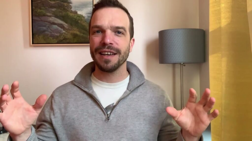 A man in grey sweater standing next to lamp.