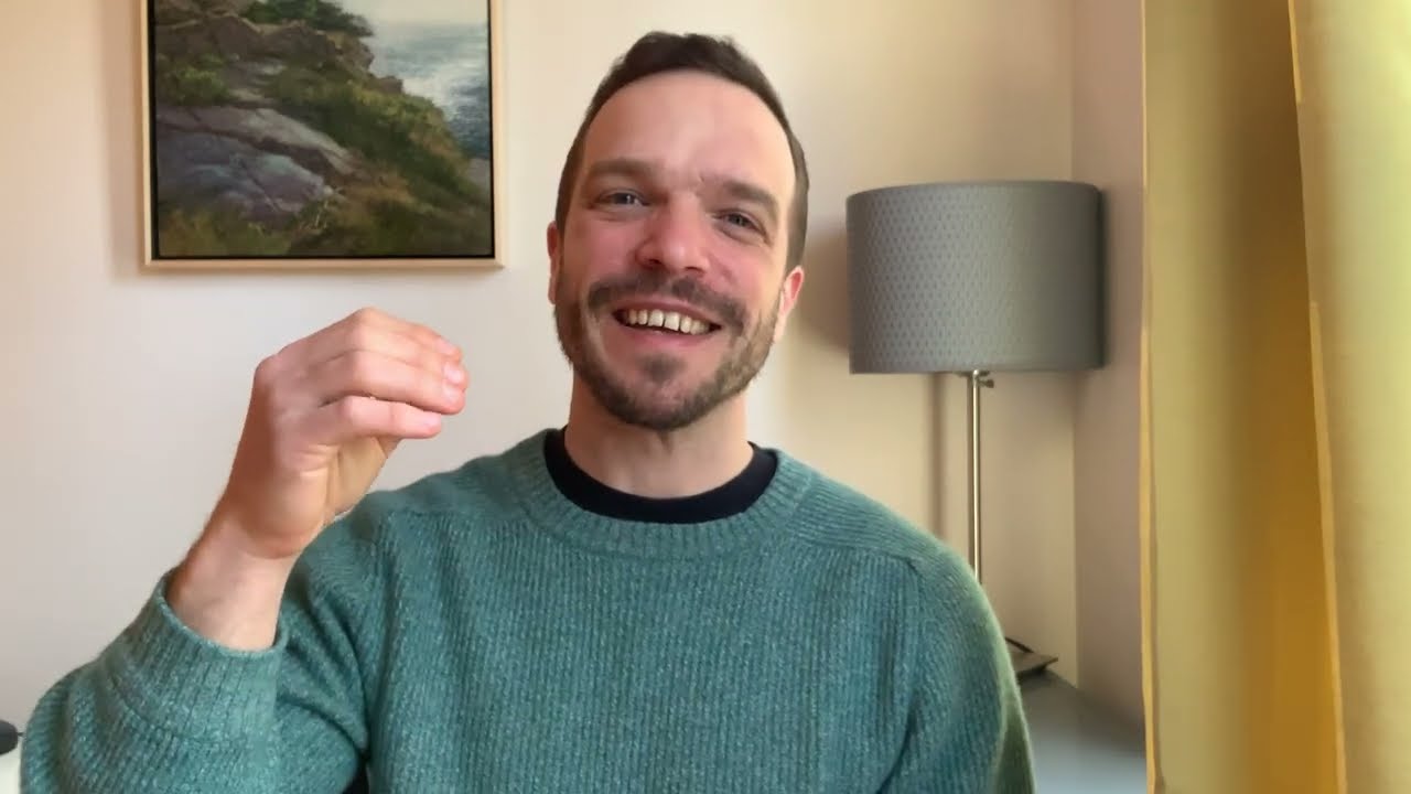 A man in green sweater holding up his hand.