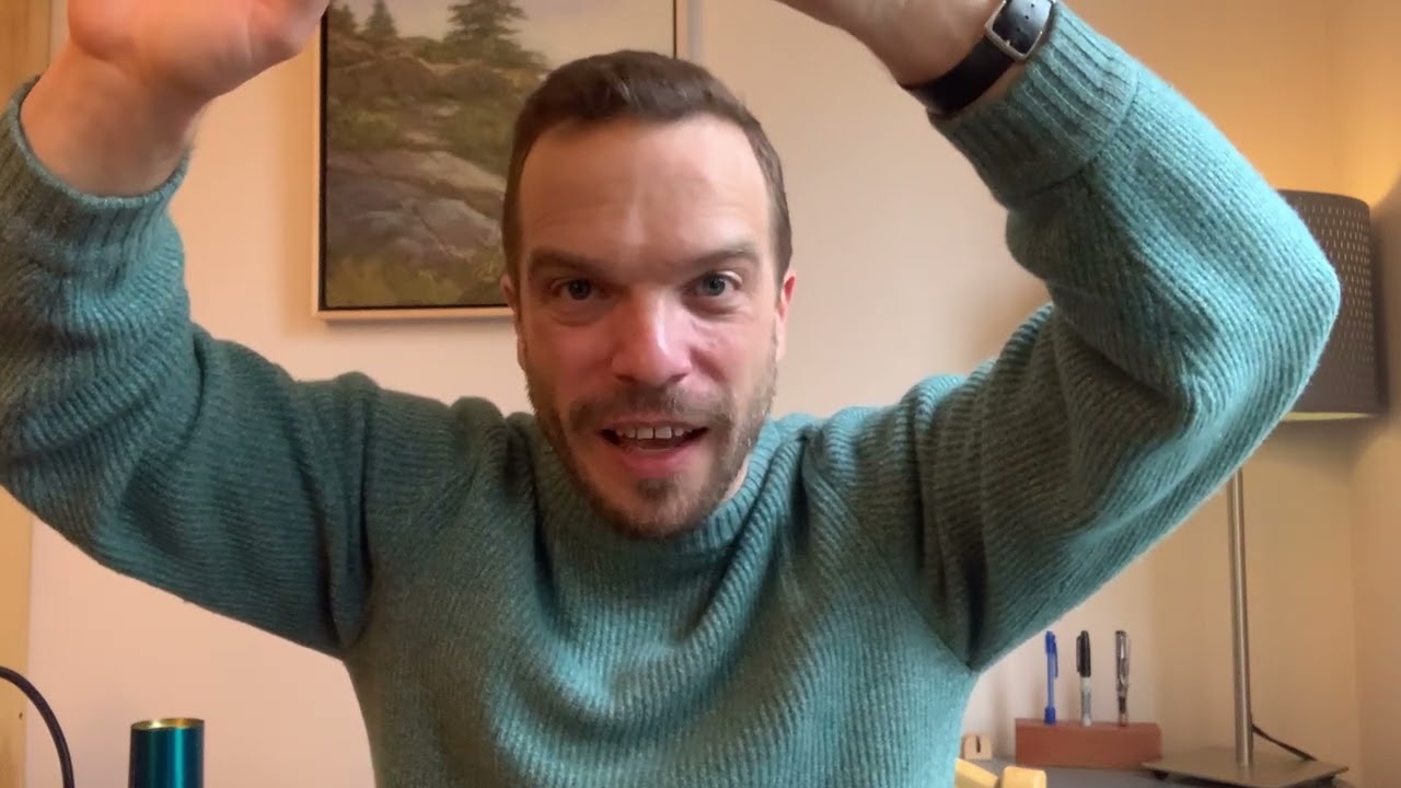 A man in a blue sweater is holding his arms up.