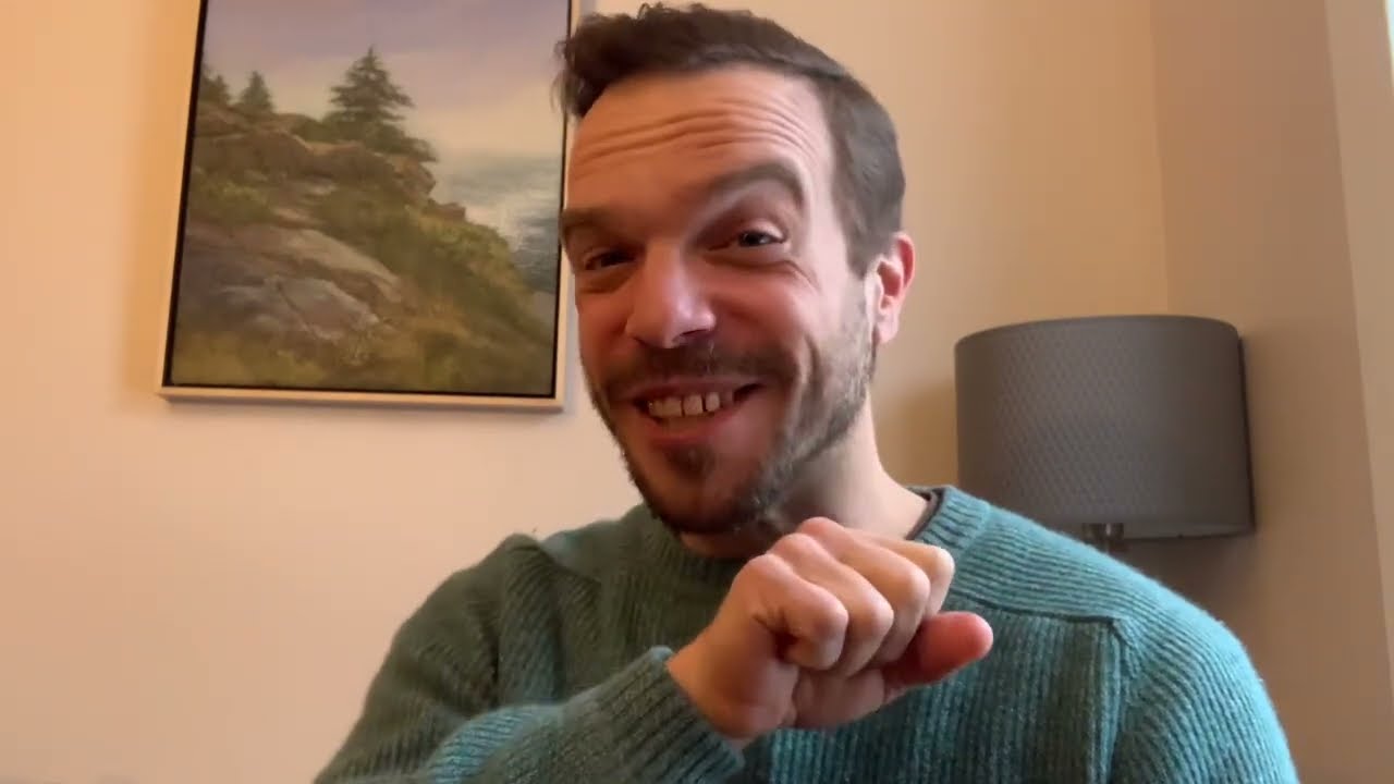 A man in a green sweater smiling for the camera.