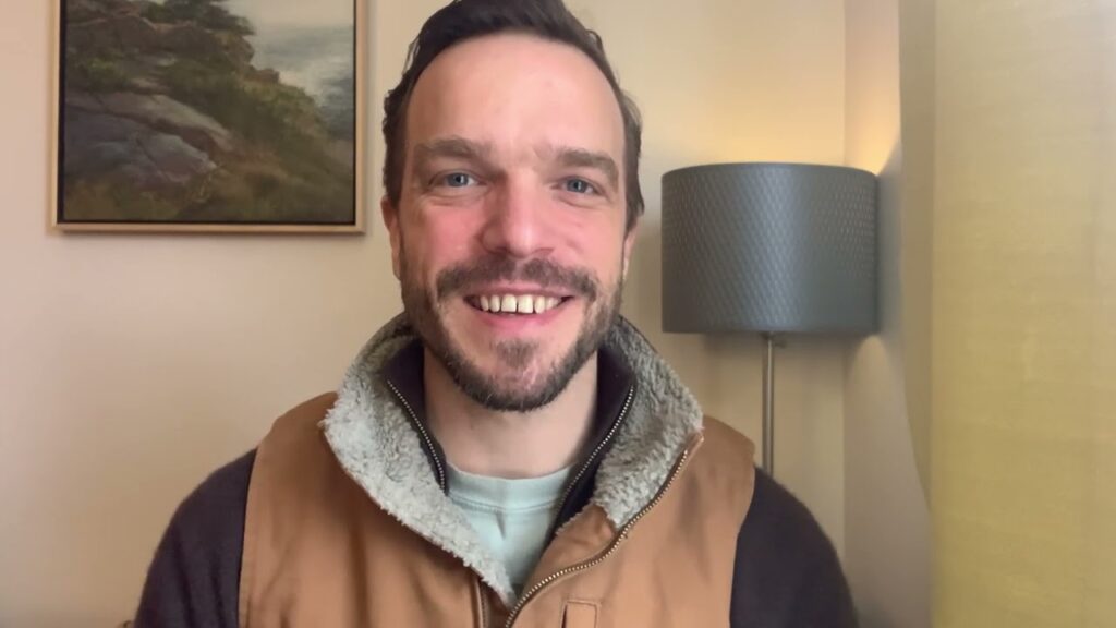 A man smiling for the camera in front of a lamp.