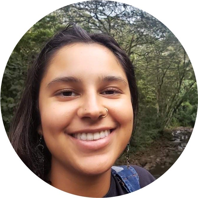 A woman smiling for the camera in front of trees.